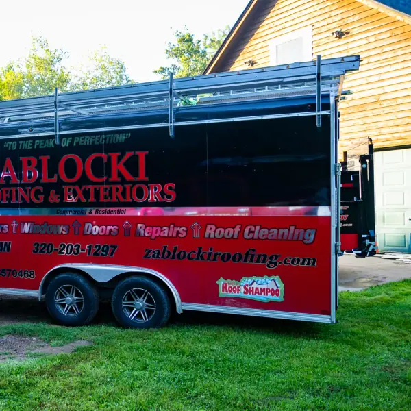Red and black Zablocki Roofing and Exteriors equipment trailer parked at a job site.