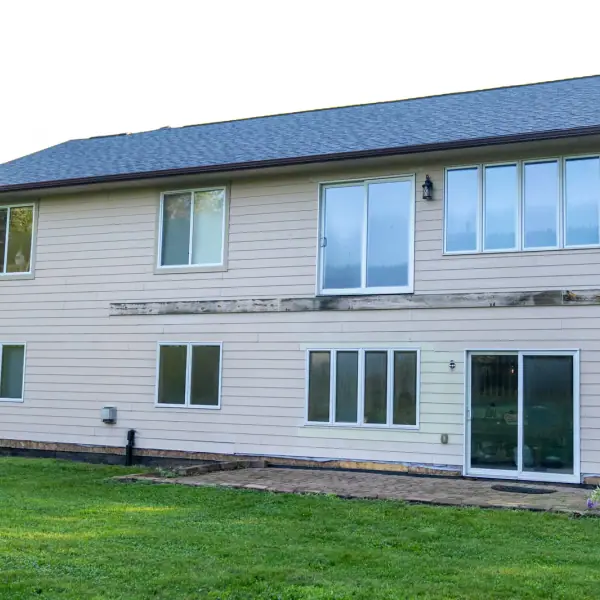 Rear of a home with new cream lap siding, white windows and a sliding patio door.