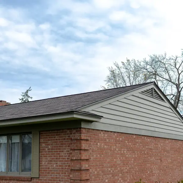 Gable end with sage lap siding, a gable vent, and new shingles above a brick wall.