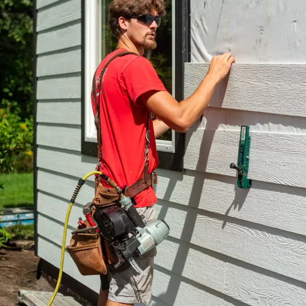 An installer positions a white lap siding plank next to a black-trimmed window over exposed house wrap.